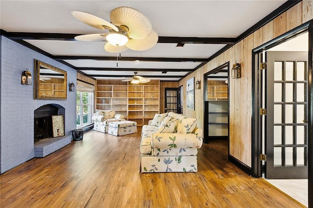 unfurnished living room with ceiling fan, wood finished floors, wood walls, a brick fireplace, and beam ceiling