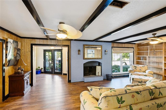 living area with a ceiling fan, wood finished floors, beamed ceiling, wood walls, and a fireplace