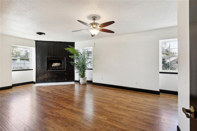 unfurnished living room with a ceiling fan, a textured ceiling, baseboards, and wood finished floors