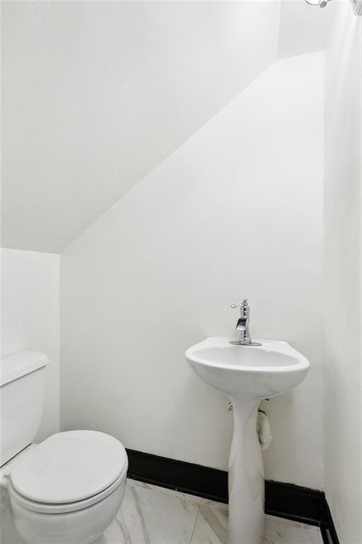 half bathroom with marble finish floor, baseboards, vaulted ceiling, and toilet