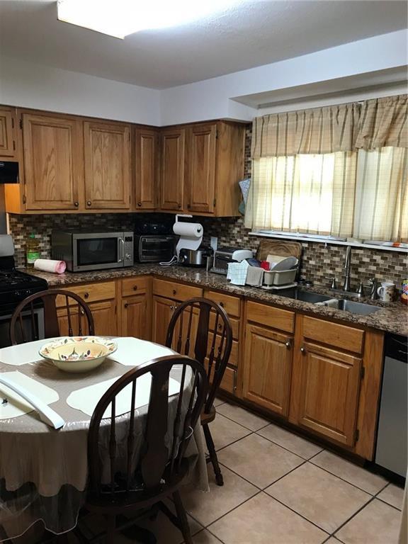 kitchen featuring light tile patterned floors, decorative backsplash, appliances with stainless steel finishes, brown cabinetry, and dark stone counters