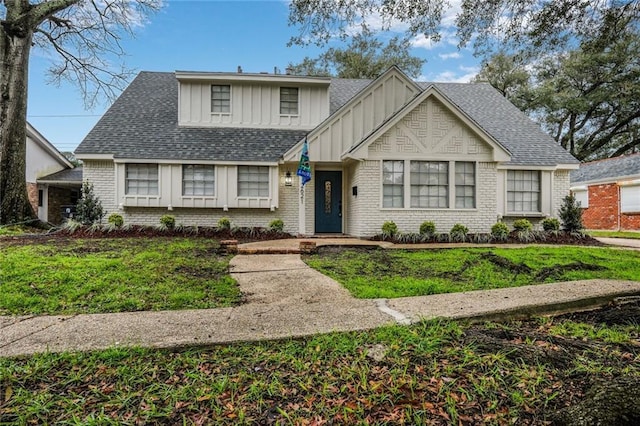 view of front of property featuring roof with shingles, a front lawn, board and batten siding, and brick siding