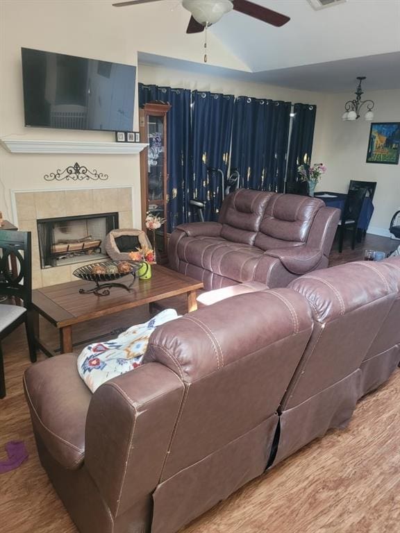 living room with ceiling fan, wood finished floors, visible vents, vaulted ceiling, and a tiled fireplace