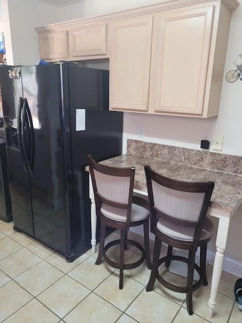 kitchen with light tile patterned floors, black refrigerator with ice dispenser, dark stone counters, a peninsula, and a kitchen bar