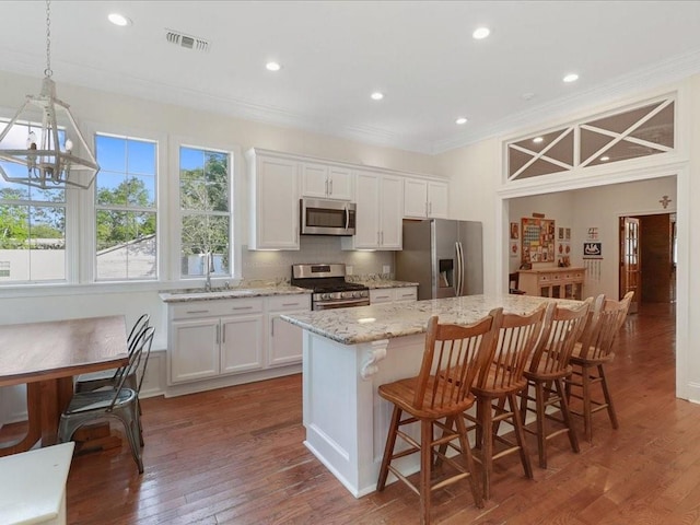 kitchen featuring white cabinets, dark wood finished floors, a kitchen island, a kitchen breakfast bar, and stainless steel appliances