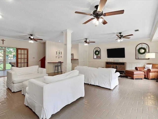 living room featuring brick floor, wainscoting, visible vents, and ornate columns