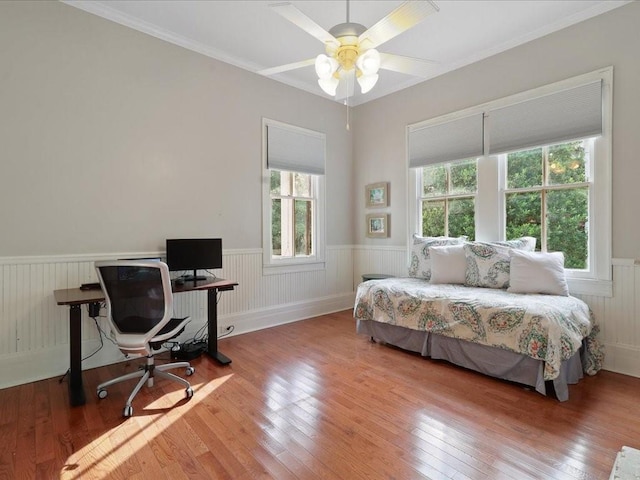 bedroom with ornamental molding, light wood finished floors, wainscoting, and a ceiling fan