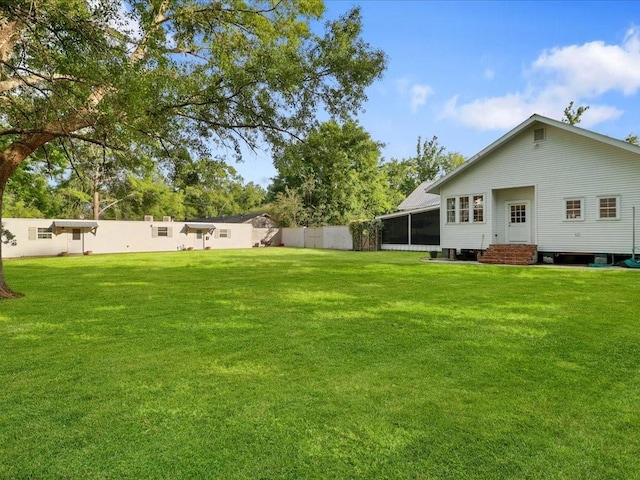 view of yard with entry steps, a sunroom, and a fenced backyard