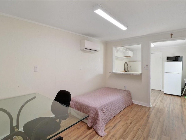 bedroom with an AC wall unit, light wood finished floors, freestanding refrigerator, and crown molding