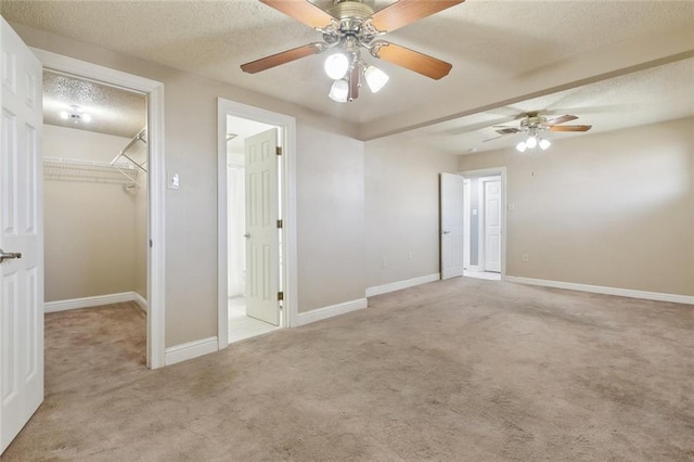 unfurnished bedroom featuring light carpet, a textured ceiling, a walk in closet, and baseboards