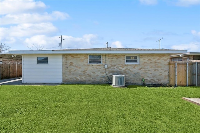 back of property with central AC, a lawn, brick siding, and fence