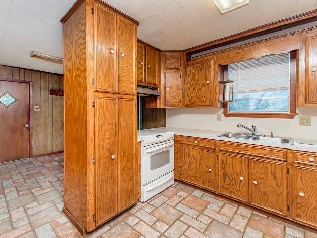 kitchen featuring light countertops, brown cabinetry, a sink, and white electric range oven