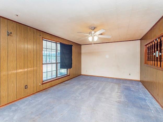 unfurnished room with light carpet, ceiling fan, and wooden walls