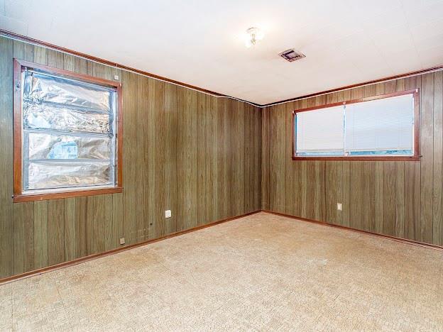 unfurnished room featuring light colored carpet, wood walls, and visible vents