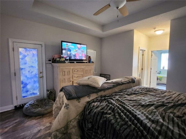 bedroom with ceiling fan, ensuite bath, a tray ceiling, and dark wood finished floors