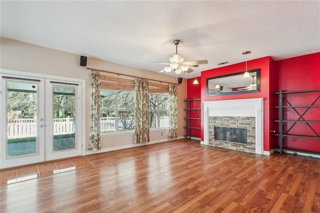 unfurnished living room with a textured ceiling, a fireplace, wood finished floors, visible vents, and french doors