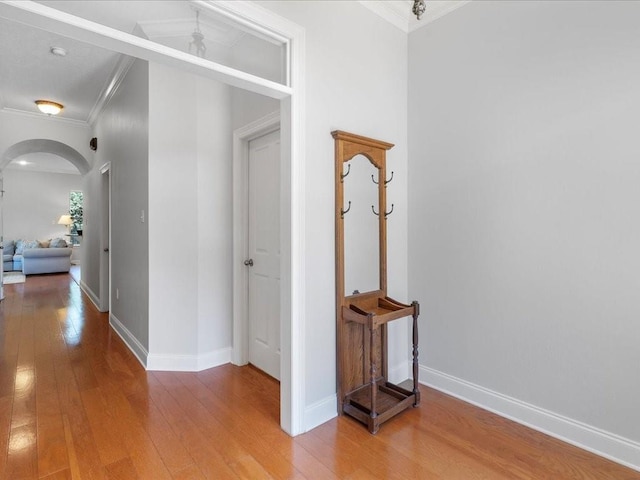 corridor featuring arched walkways, baseboards, wood finished floors, and crown molding