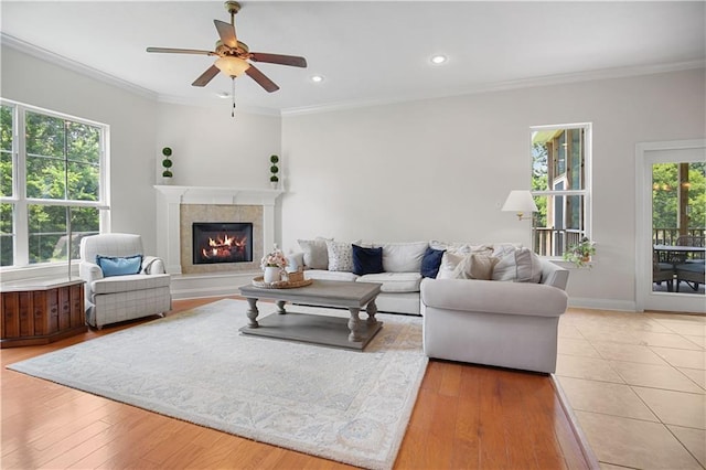 living room with crown molding, recessed lighting, a tiled fireplace, wood finished floors, and baseboards