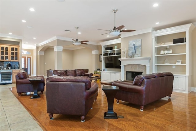 living room featuring wine cooler, arched walkways, crown molding, recessed lighting, and a tiled fireplace