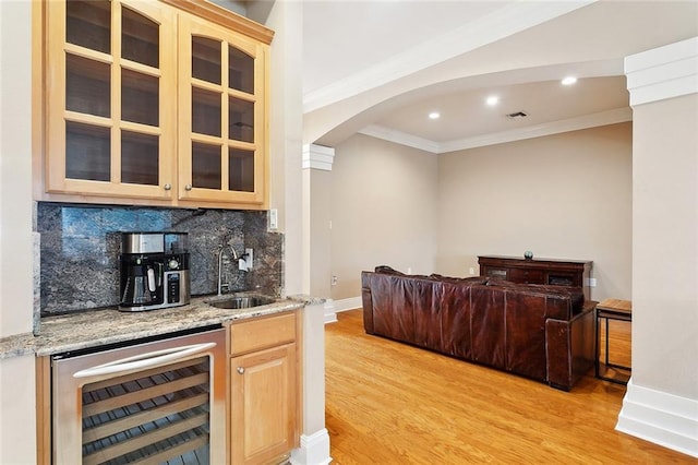 indoor wet bar with beverage cooler, ornamental molding, light wood finished floors, arched walkways, and tasteful backsplash