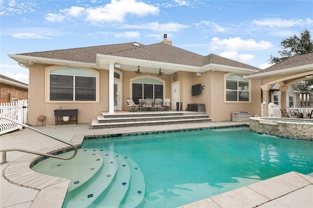 rear view of property featuring a patio, stucco siding, a chimney, fence, and a pool with connected hot tub