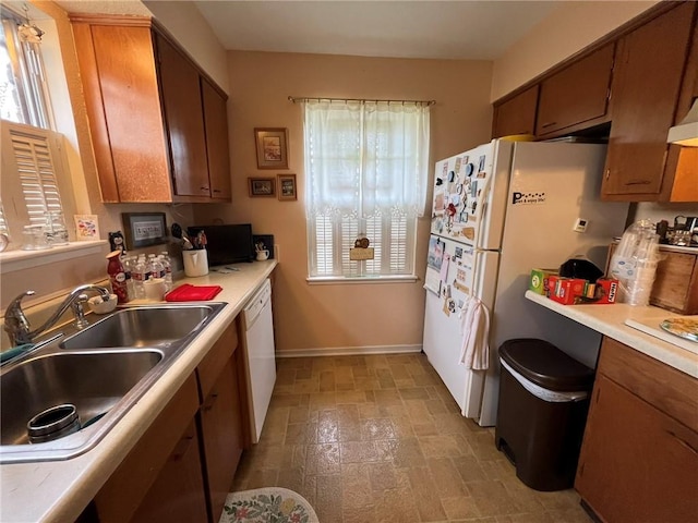 kitchen with brown cabinets, white appliances, light countertops, and a sink