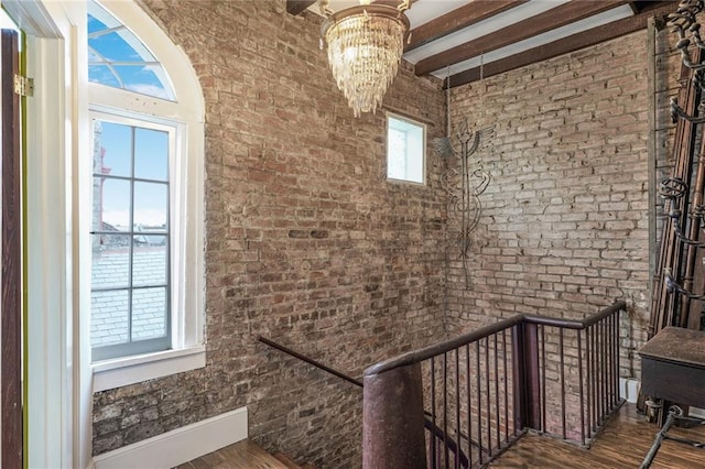 stairs featuring brick wall, beam ceiling, a chandelier, and wood finished floors