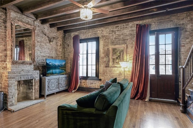 living room featuring a fireplace with raised hearth, brick wall, wood finished floors, stairs, and beam ceiling