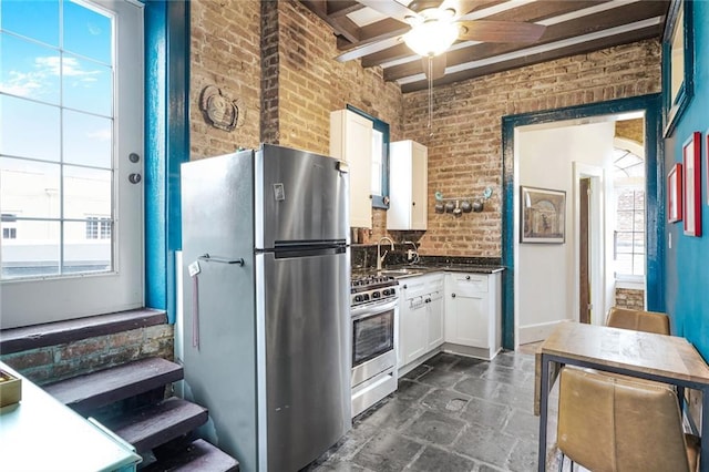 kitchen featuring stainless steel appliances, brick wall, a sink, white cabinetry, and dark countertops