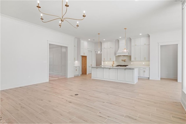 kitchen featuring a center island with sink, white cabinets, decorative light fixtures, light countertops, and premium range hood