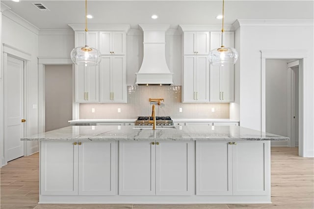 kitchen featuring light stone countertops, custom range hood, a center island with sink, and white cabinets