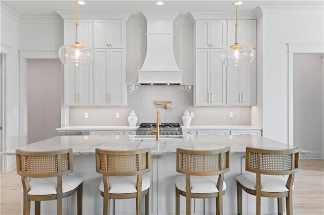 4221 Cypress Point Dr, Covington, LA 70433 - kitchen with light wood-style floors, a center island with sink, hanging light fixtures, and custom exhaust hood