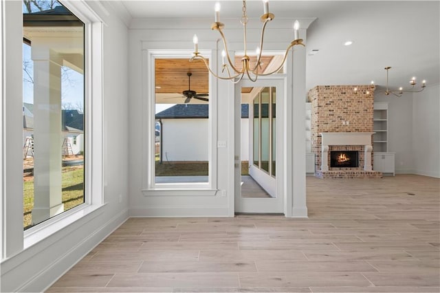 unfurnished dining area featuring a brick fireplace, light wood-style flooring, a chandelier, and baseboards