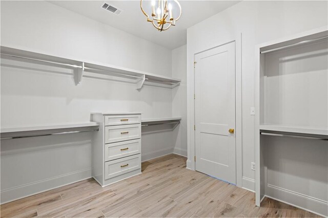 walk in closet with light wood-style floors, visible vents, and a notable chandelier