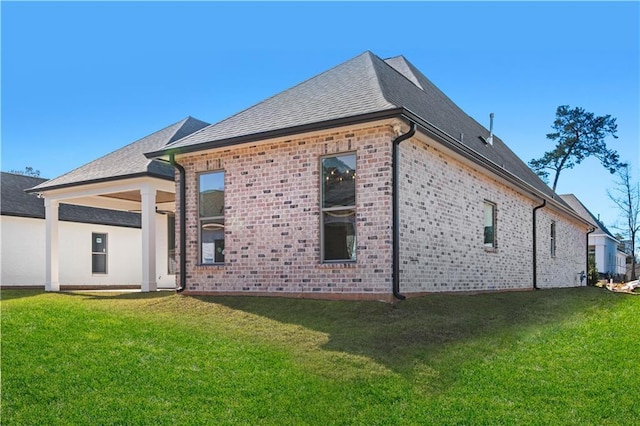 rear view of property featuring a yard, brick siding, and a shingled roof