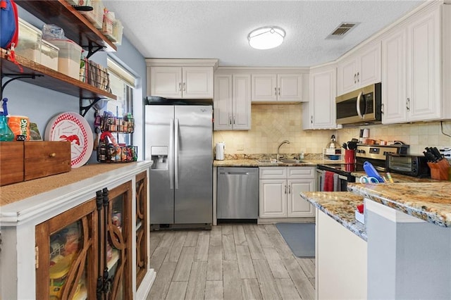 kitchen featuring light stone counters, stainless steel appliances, visible vents, white cabinetry, and a sink