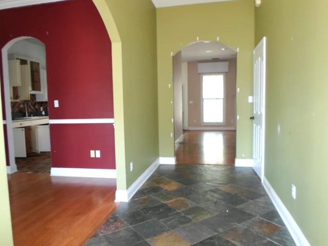 hall with arched walkways, stone finish flooring, and baseboards