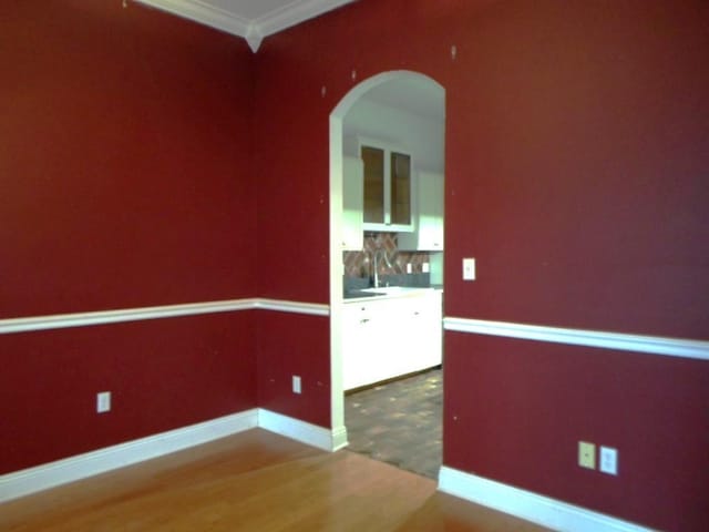 empty room featuring arched walkways, ornamental molding, wood finished floors, and baseboards