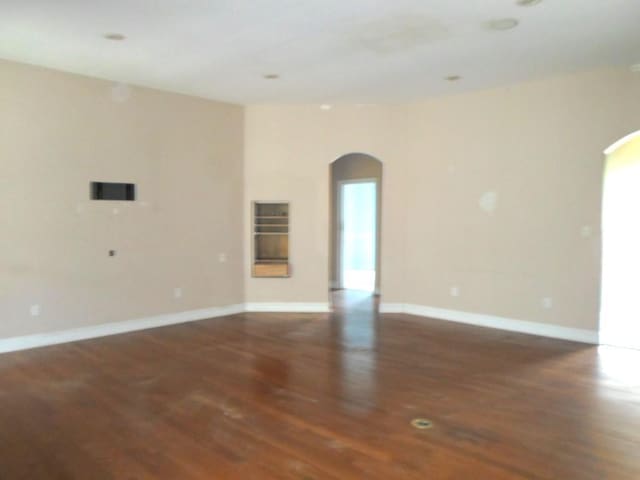 unfurnished room with baseboards, arched walkways, and dark wood-style flooring