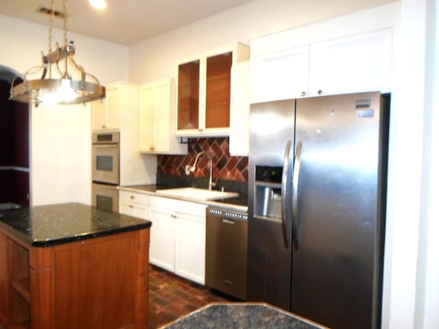 kitchen with dark stone counters, a sink, stainless steel appliances, white cabinetry, and backsplash