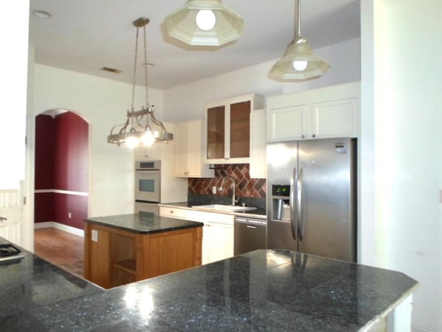 kitchen featuring arched walkways, white cabinets, appliances with stainless steel finishes, pendant lighting, and a sink