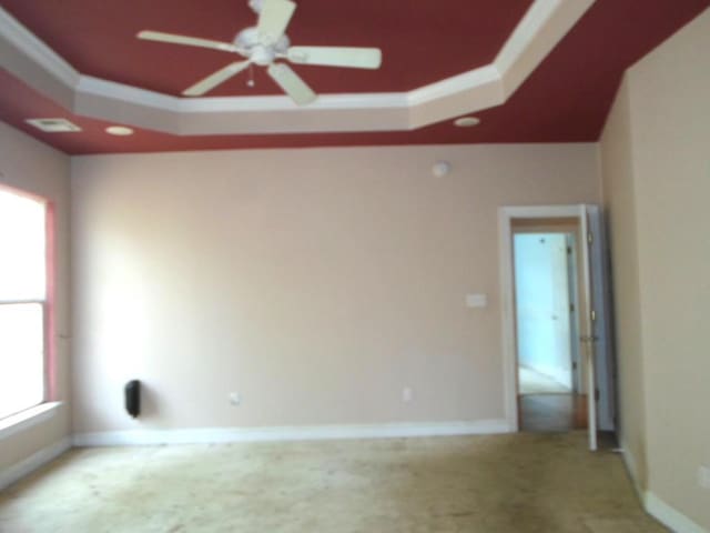 carpeted spare room with ceiling fan, baseboards, a raised ceiling, and crown molding