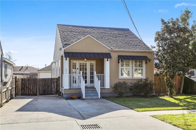 bungalow-style home with stucco siding, fence, a front lawn, and roof with shingles