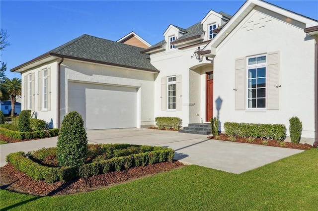 view of front of home with driveway, roof with shingles, an attached garage, a front lawn, and stucco siding