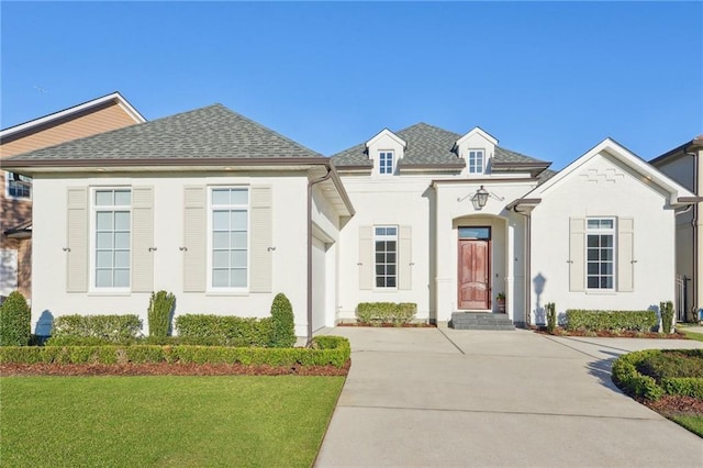 french country style house featuring a shingled roof, a front yard, and stucco siding