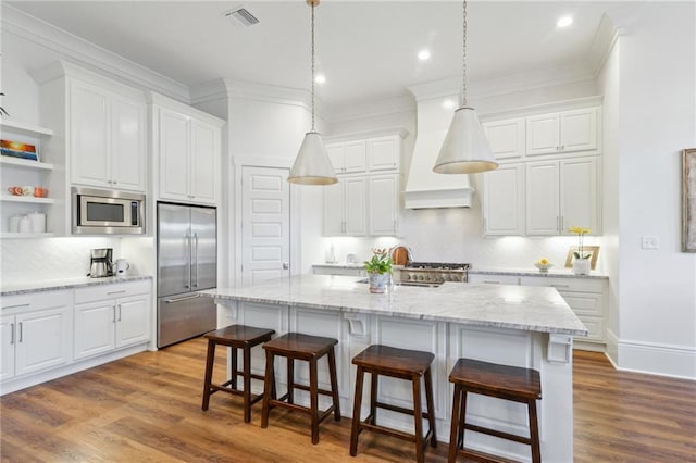 kitchen featuring visible vents, an island with sink, decorative light fixtures, built in appliances, and white cabinetry