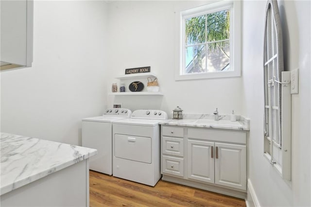 clothes washing area with cabinet space, a sink, light wood finished floors, and separate washer and dryer