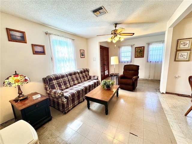 living area featuring a ceiling fan, visible vents, a textured ceiling, and baseboards