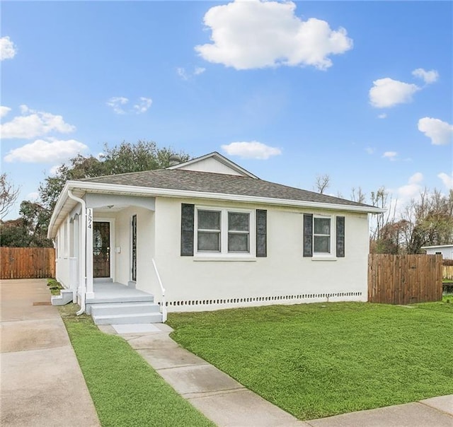 view of front of house featuring a front lawn, roof with shingles, fence, and stucco siding