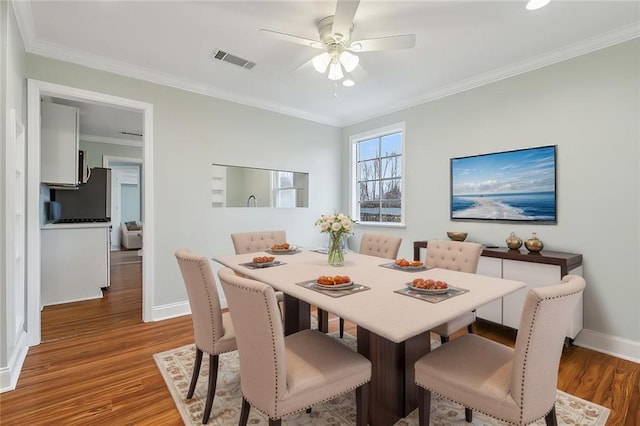 dining area with visible vents, ornamental molding, ceiling fan, wood finished floors, and baseboards